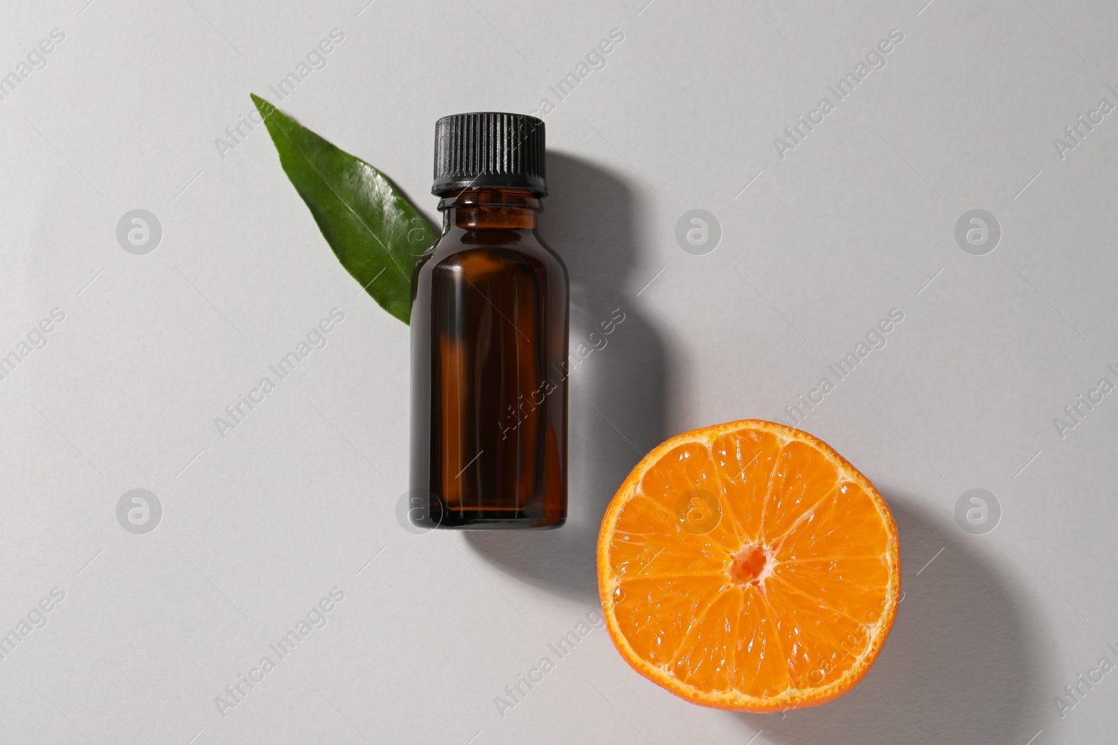 Photo of Aromatic tangerine essential oil in bottle, leaf and citrus fruit on grey table, top view