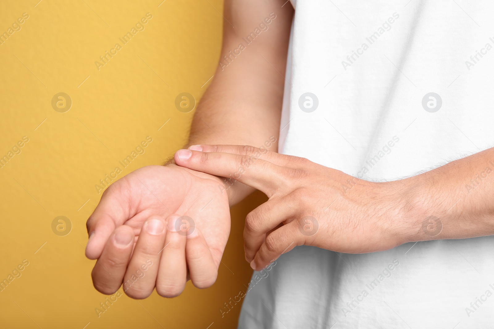Photo of Young man checking pulse on color background