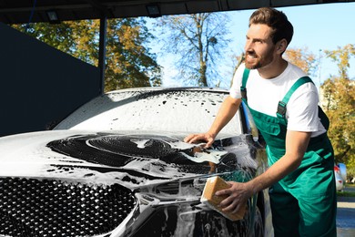 Worker washing auto with sponge at outdoor car wash