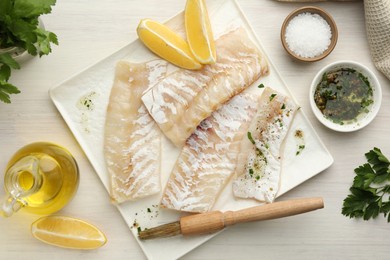 Photo of Fresh raw cod fillets with spices and lemon on white wooden table, flat lay