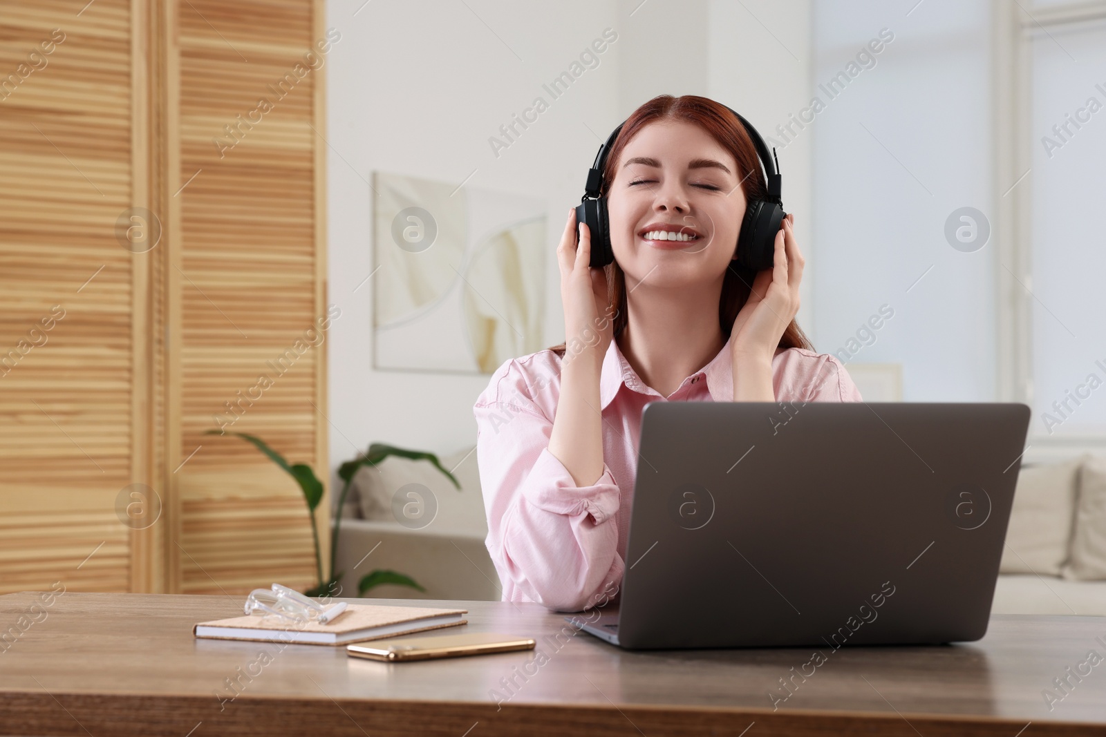 Photo of Happy woman with headphones listening to music and laptop on wooden table