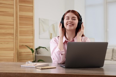 Photo of Happy woman with headphones listening to music and laptop on wooden table