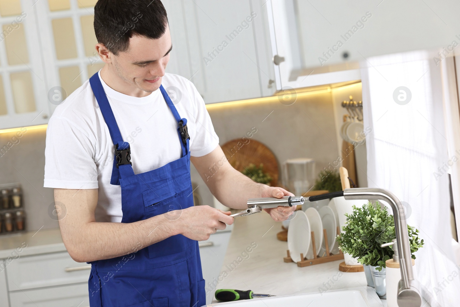 Photo of Young plumber repairing faucet with spanner in kitchen