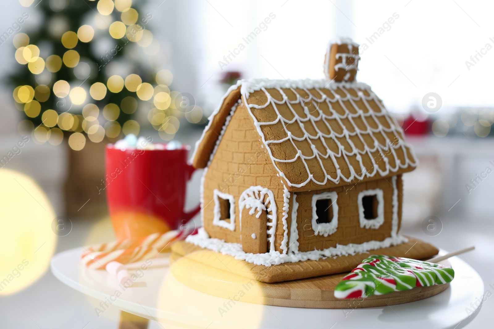 Photo of Beautiful gingerbread house decorated with icing on white table indoors