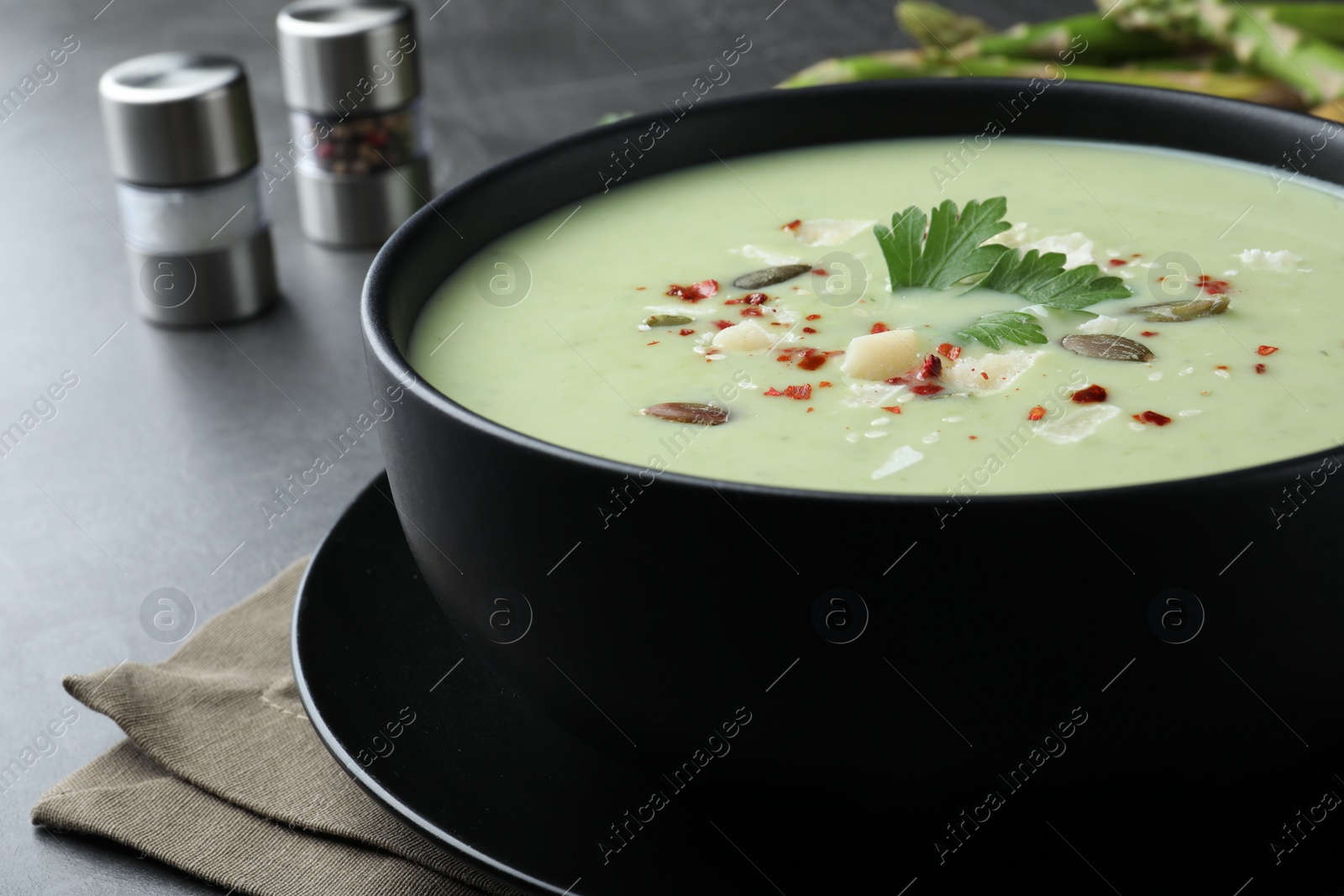 Photo of Bowl of delicious asparagus soup on dark table, closeup