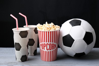 Photo of Football ball with popcorn and cups on grey wooden table