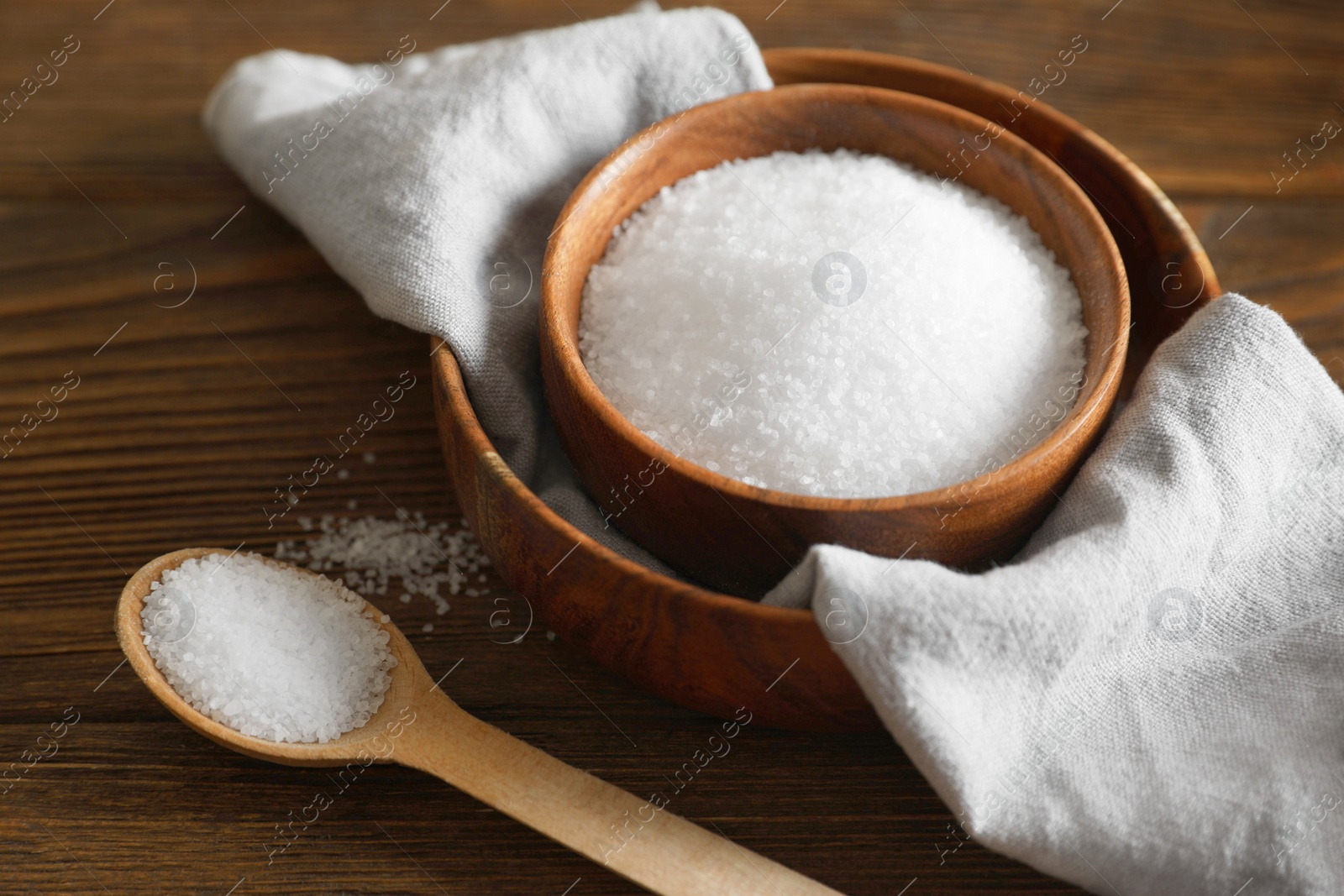 Photo of Organic salt in bowl and spoon on wooden table, closeup