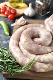 Photo of Raw homemade sausage, rosemary and other products on grey textured table, closeup