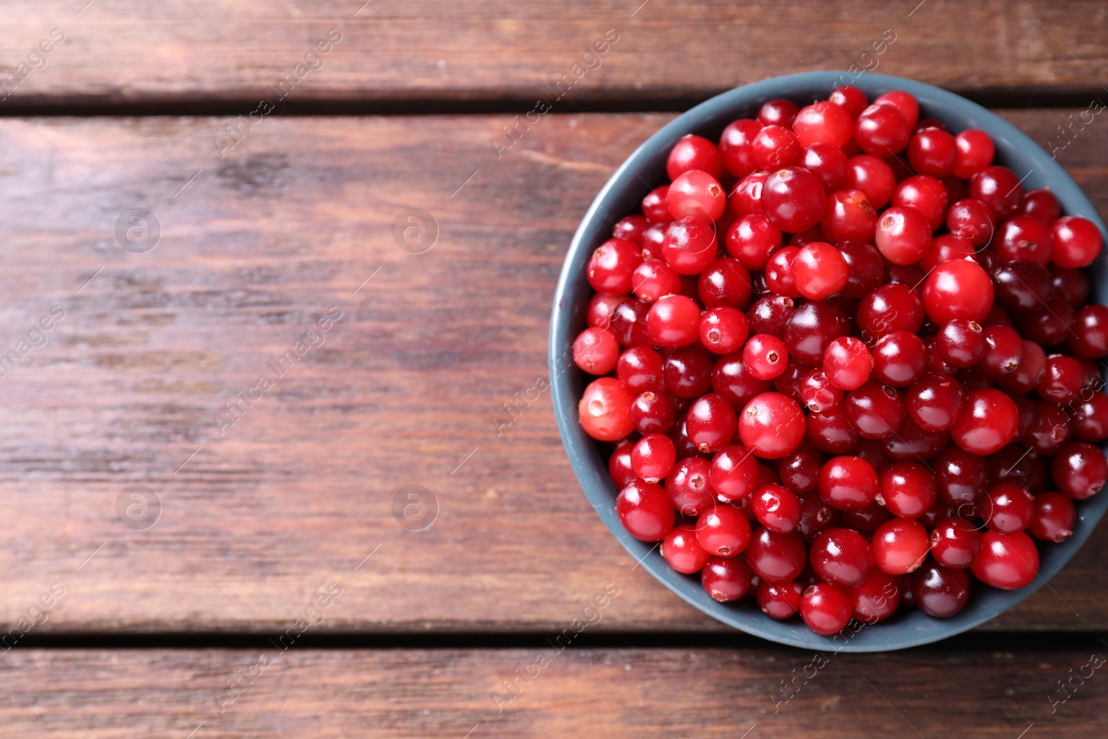 Photo of Fresh ripe cranberries in bowl on wooden table, top view. Space for text