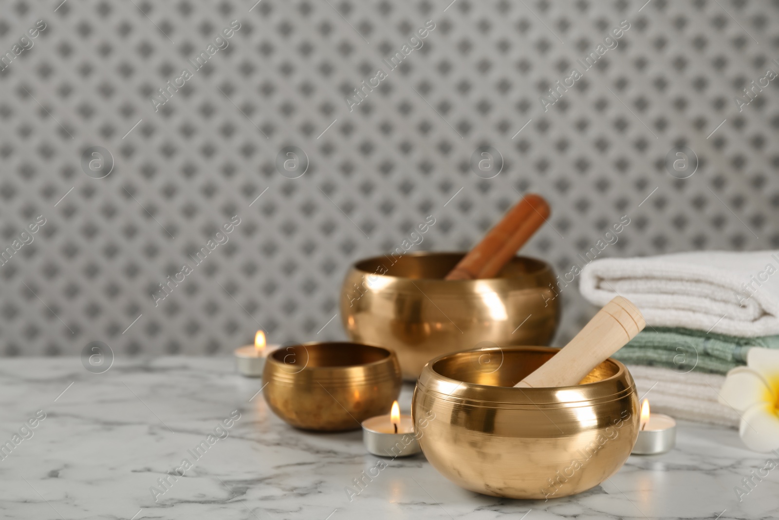 Photo of Tibetan singing bowls, mallets, towels and burning candles on white marble table, space for text