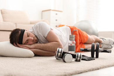 Lazy young man with sport equipment sleeping on floor at home