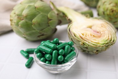 Bowl with pills and fresh artichokes on white tiled table, closeup