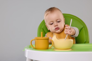 Cute little baby eating healthy food in high chair on gray background, space for text