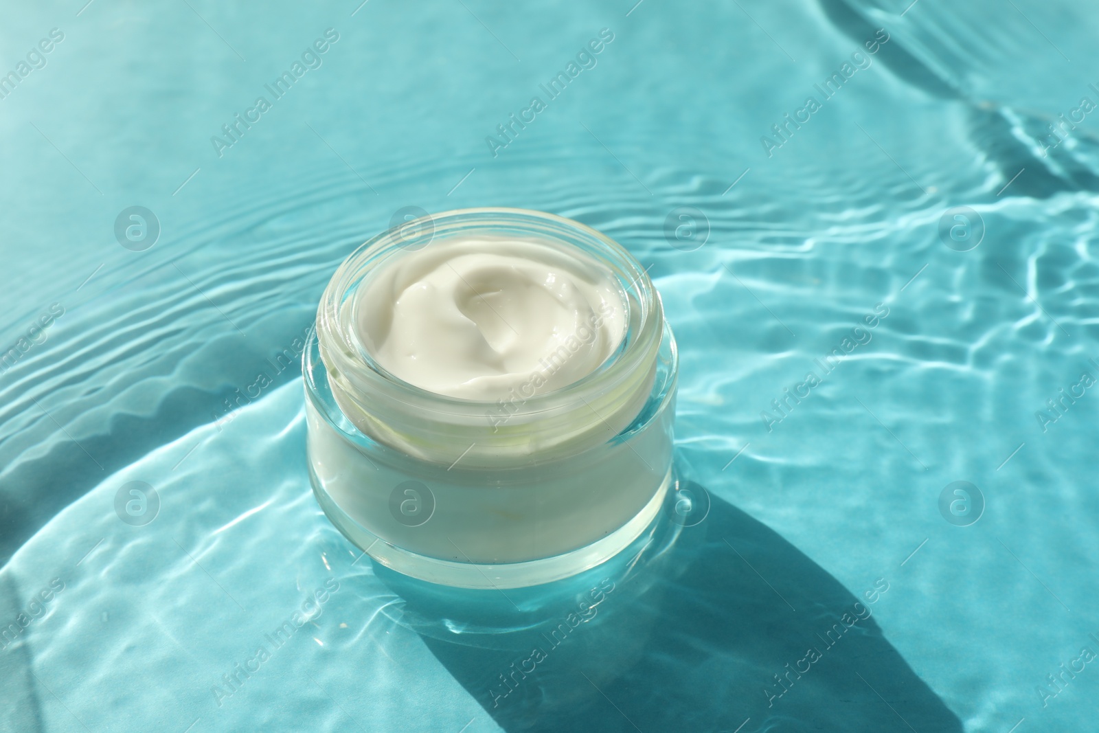 Photo of Jar with moisturizing cream in water on light blue background