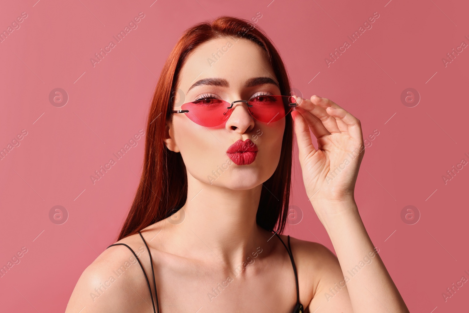 Photo of Beautiful woman with red dyed hair and sunglasses on pink background