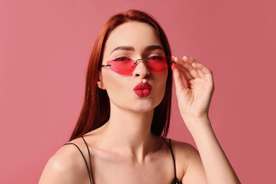 Photo of Beautiful woman with red dyed hair and sunglasses on pink background