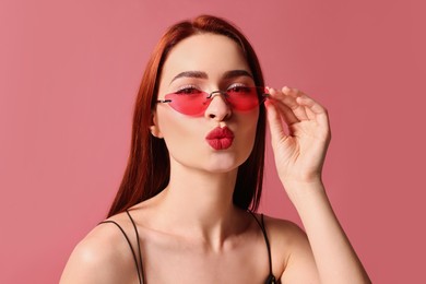 Beautiful woman with red dyed hair and sunglasses on pink background