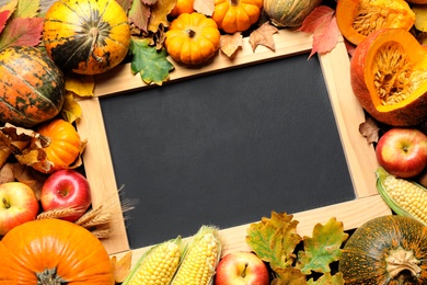 Photo of Flat lay composition with blank chalkboard, fruits, vegetables and autumn leaves as background, space for text. Thanksgiving Day