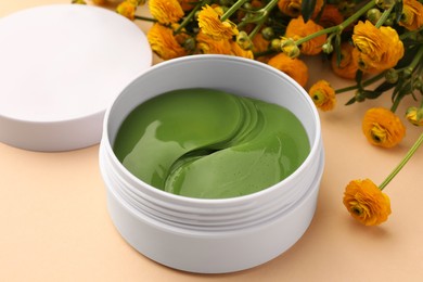 Photo of Jar of under eye patches and beautiful flowers on beige background, closeup. Cosmetic product