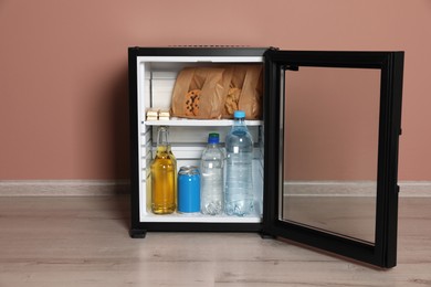 Photo of Mini bar filled with food and drinks near pale pink wall indoors