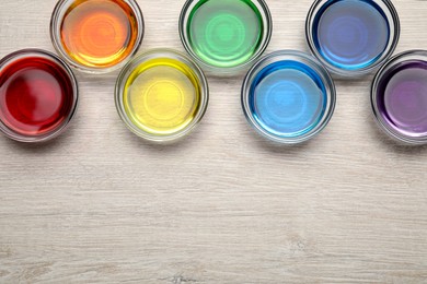 Glass bowls with different food coloring on wooden table, flat lay. Space for text