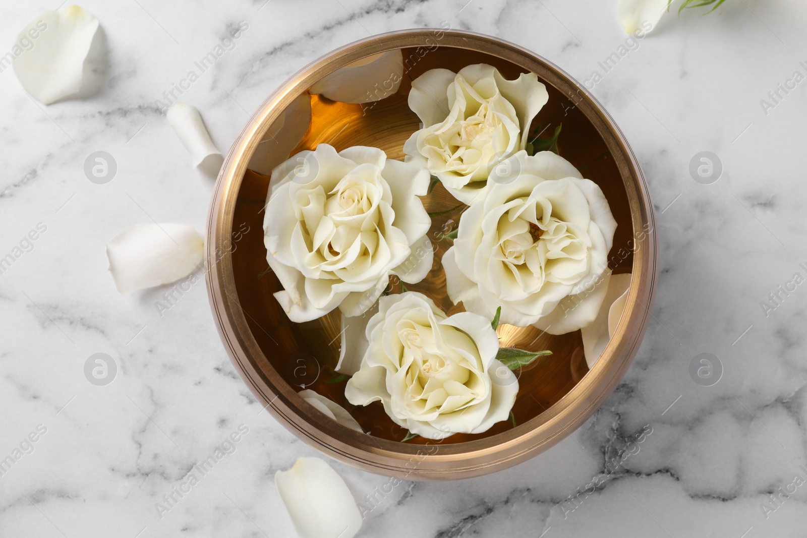 Photo of Tibetan singing bowl with water and beautiful roses on white marble table, top view