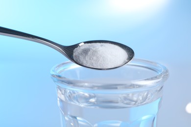 Photo of Adding baking soda into glass of water on light blue background, closeup