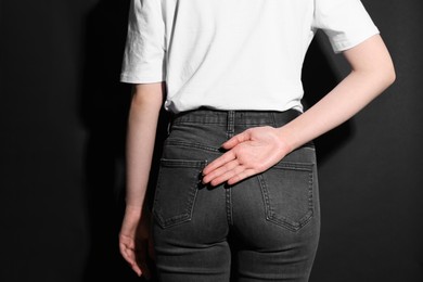 Woman showing open palm behind her back on black background, back view