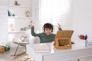 Photo of Emotional little boy with modern tablet studying online at home. E-learning