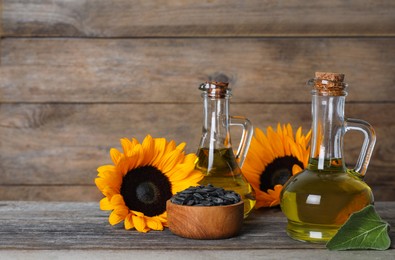 Photo of Sunflower cooking oil, seeds and yellow flowers on wooden table, space for text