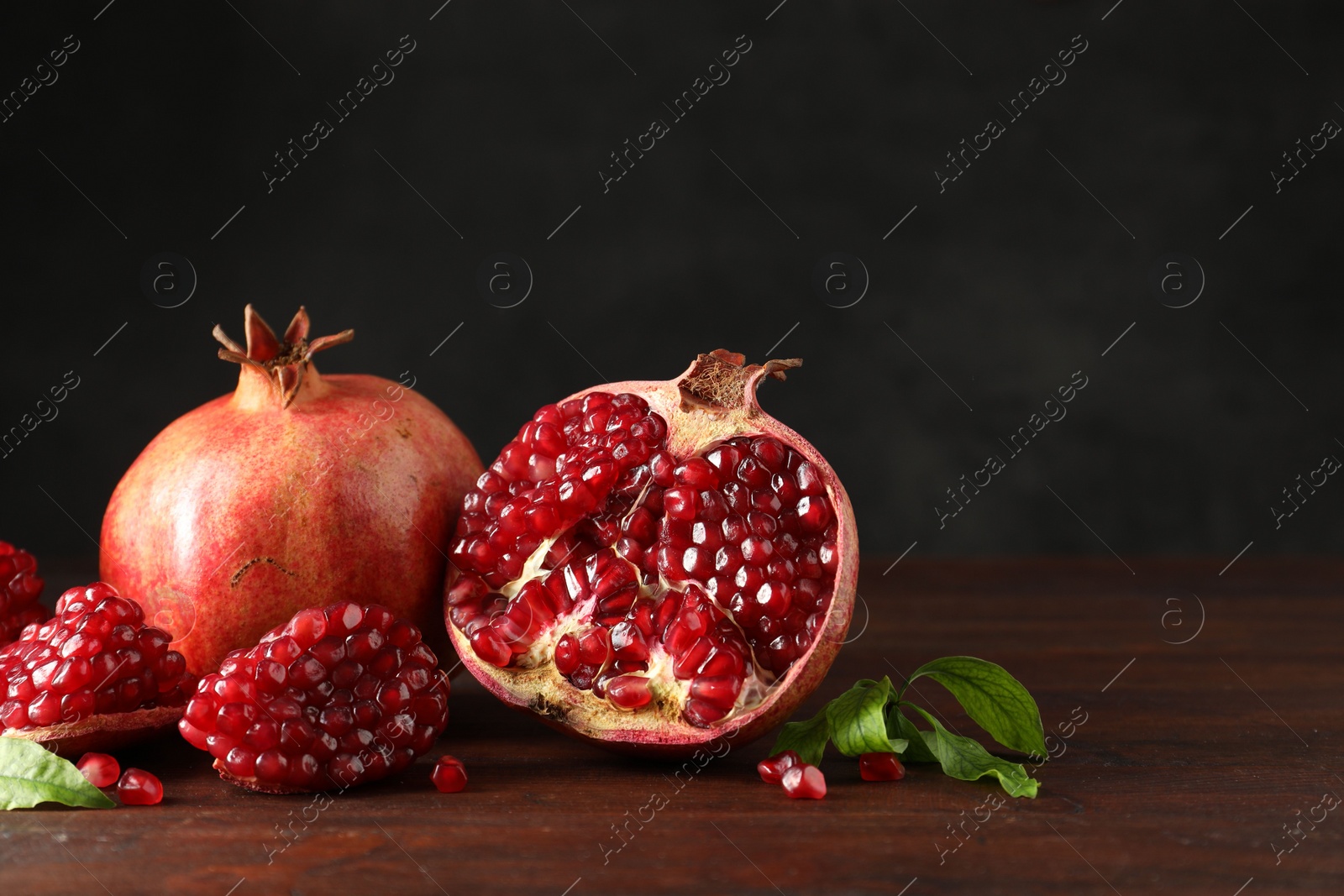 Photo of Fresh pomegranates and green leaves on wooden table, space for text