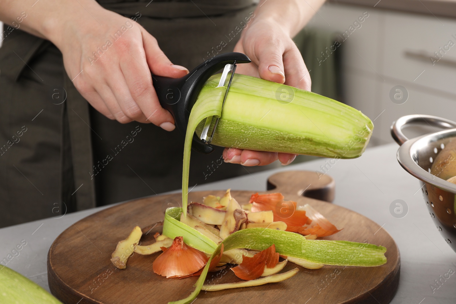 Photo of Woman peeling fresh zucchini at light table indoors, closeup