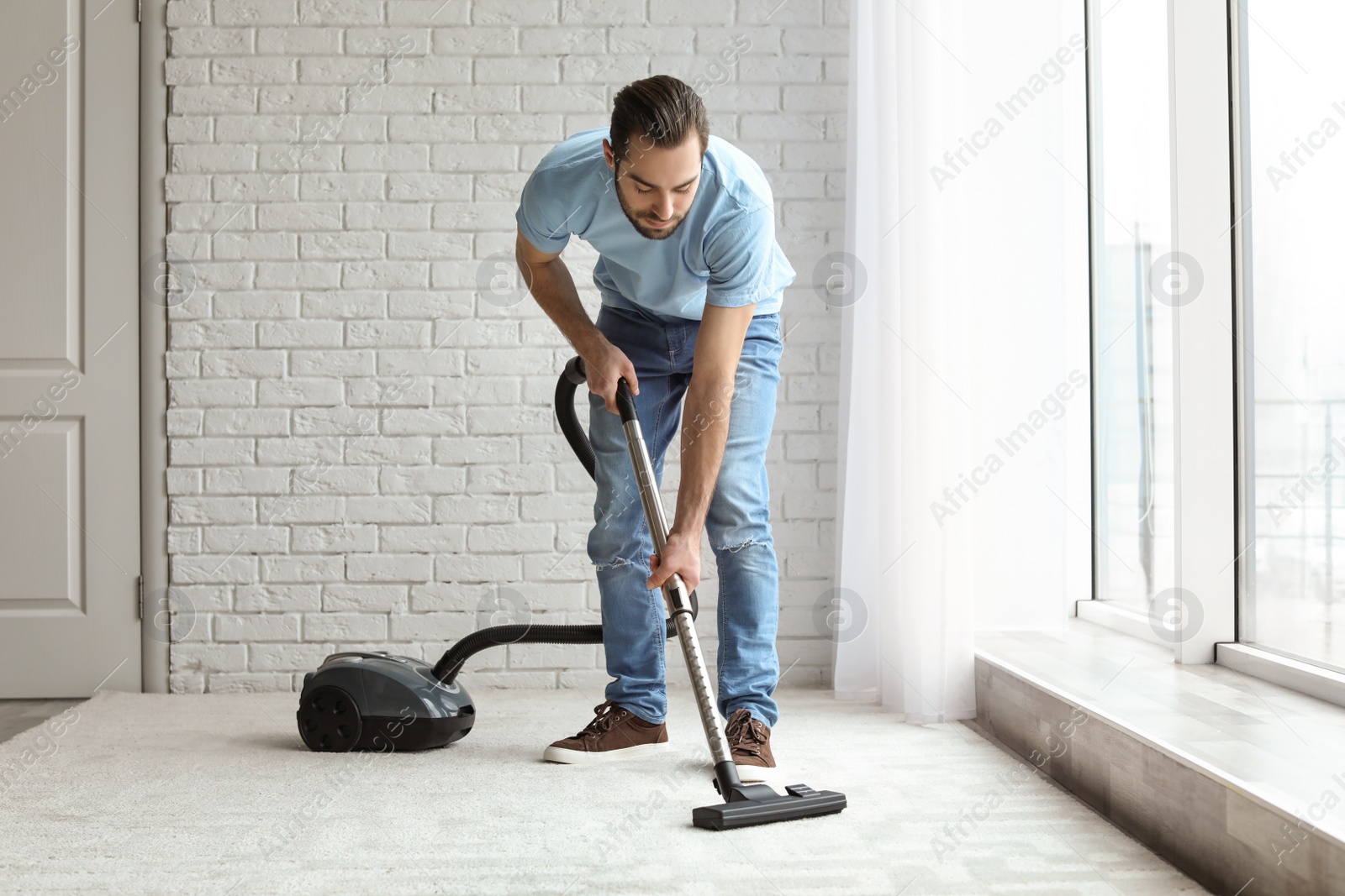 Photo of Young man cleaning carpet with vacuum at home