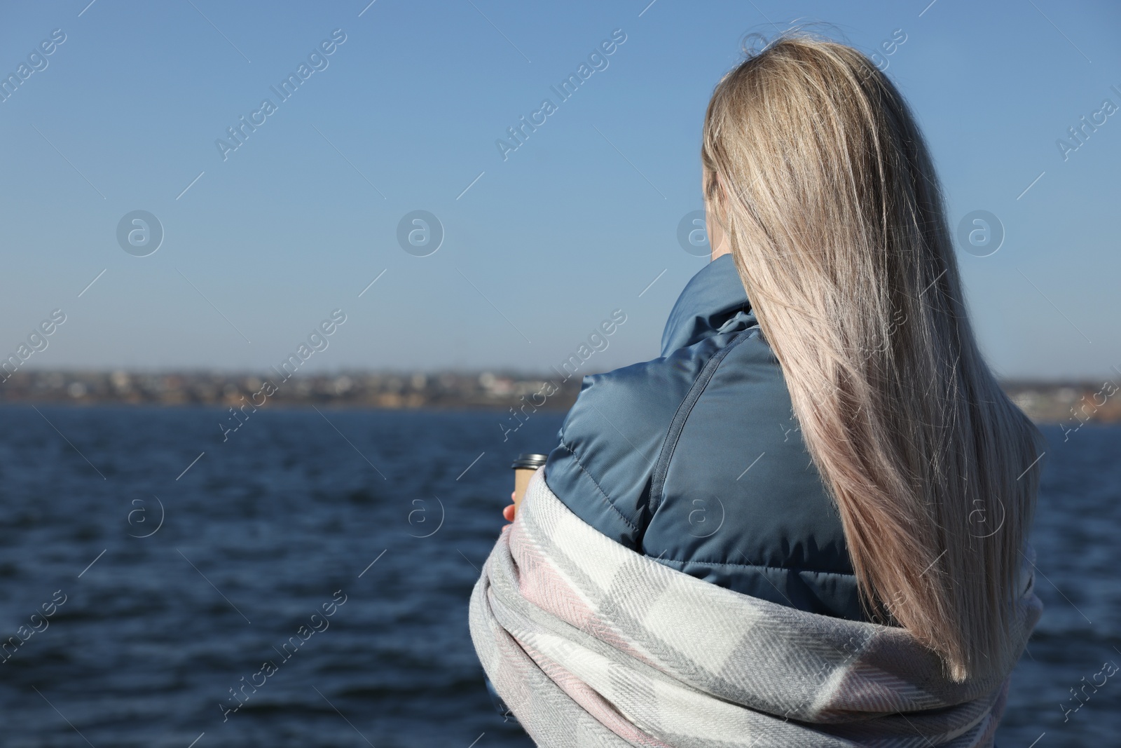 Photo of Lonely woman with cup of drink near river on sunny day, back view