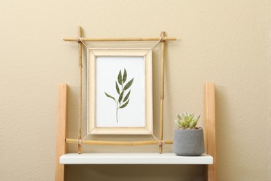 Photo of Bamboo frame and green plant on shelving unit near beige wall