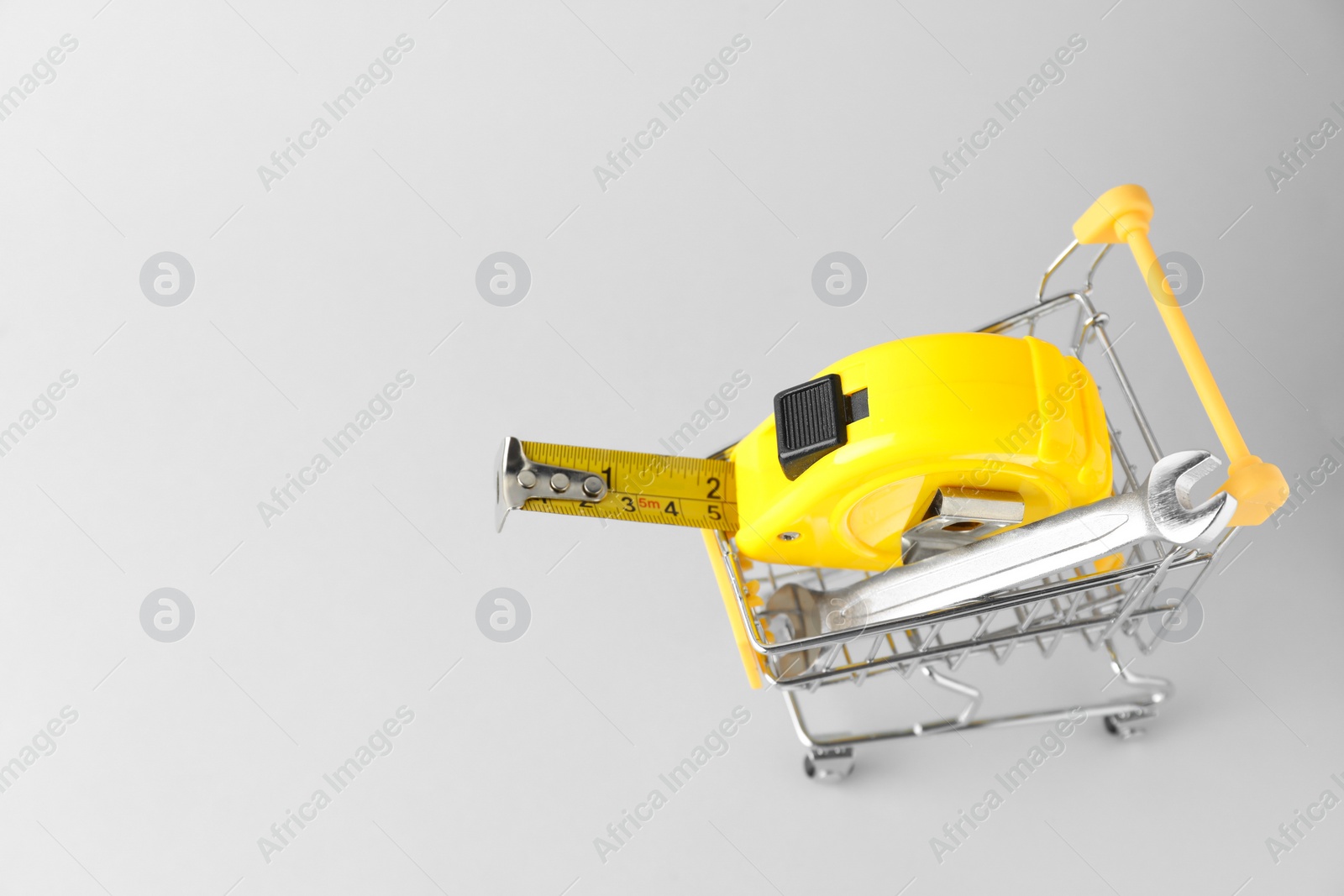 Photo of Metal wrench and measuring tape in shopping cart on light grey background, above view. Space for text