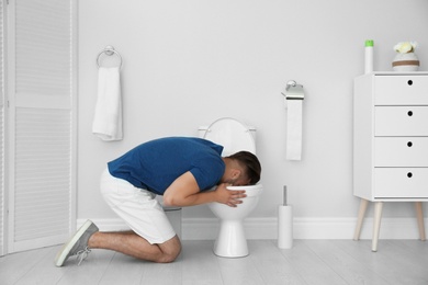 Young man vomiting in toilet bowl at home