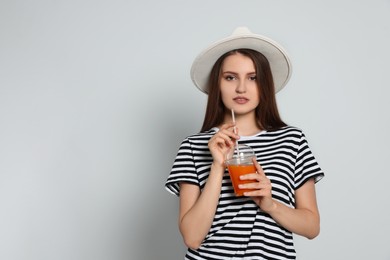 Beautiful young woman with plastic cup of juice on light grey background