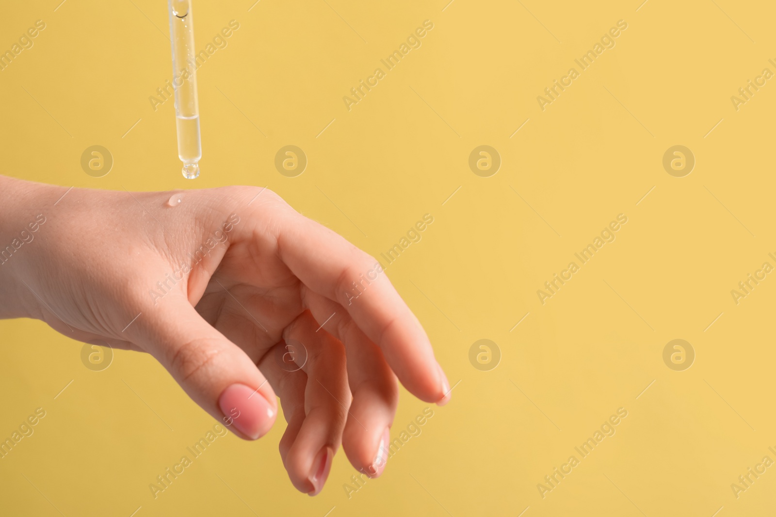 Photo of Woman dripping serum from pipette on her hand against pale orange background, closeup. Space for text