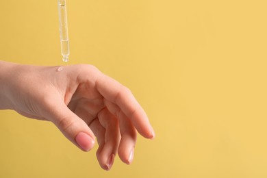 Photo of Woman dripping serum from pipette on her hand against pale orange background, closeup. Space for text
