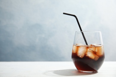 Photo of Glass of refreshing cola with ice cubes and straw on table. Space for text