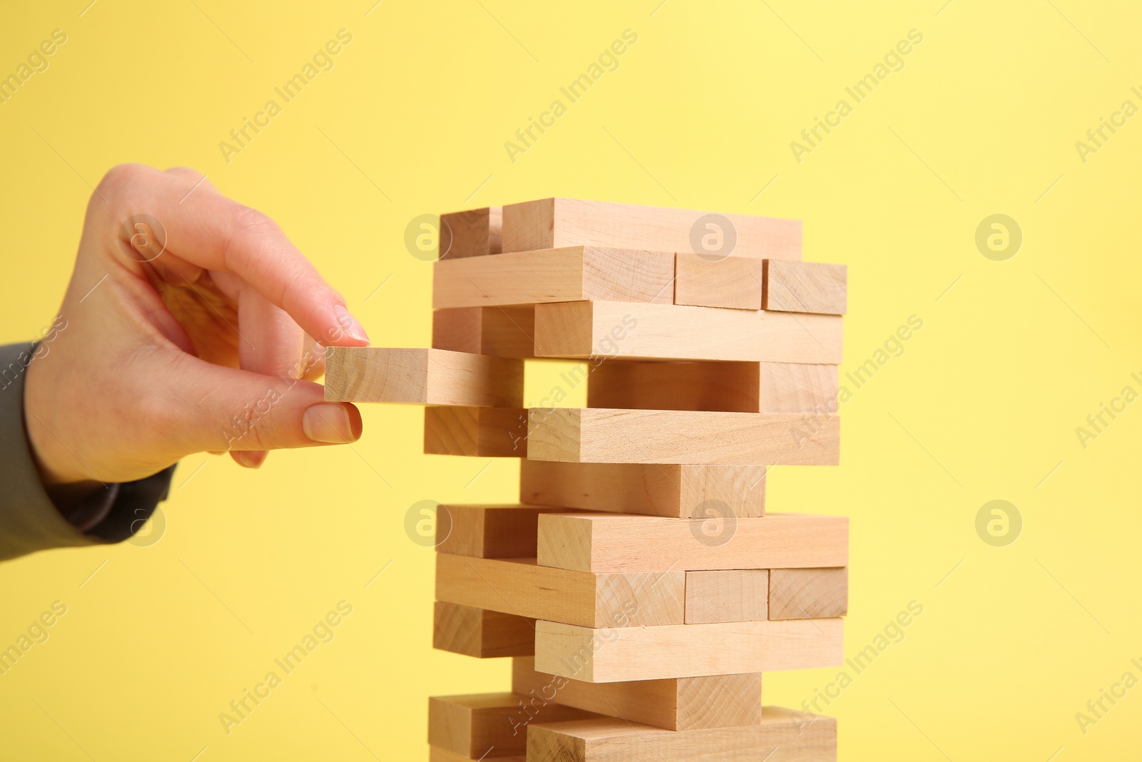 Photo of Woman playing Jenga tower on yellow background, closeup