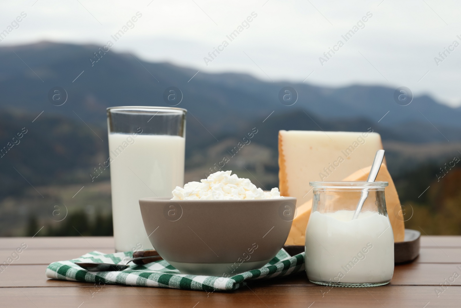 Photo of Tasty cottage cheese and other fresh dairy products on wooden table in mountains