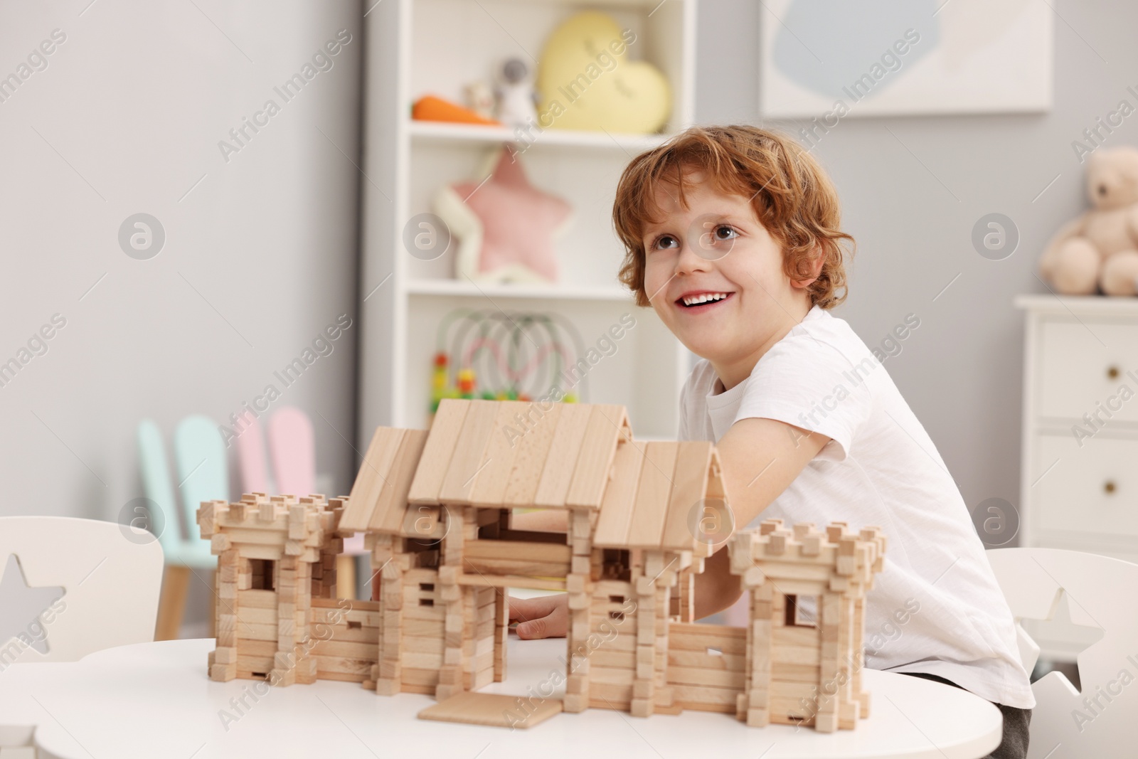 Photo of Little boy playing with wooden entry gate at white table in room. Child's toy