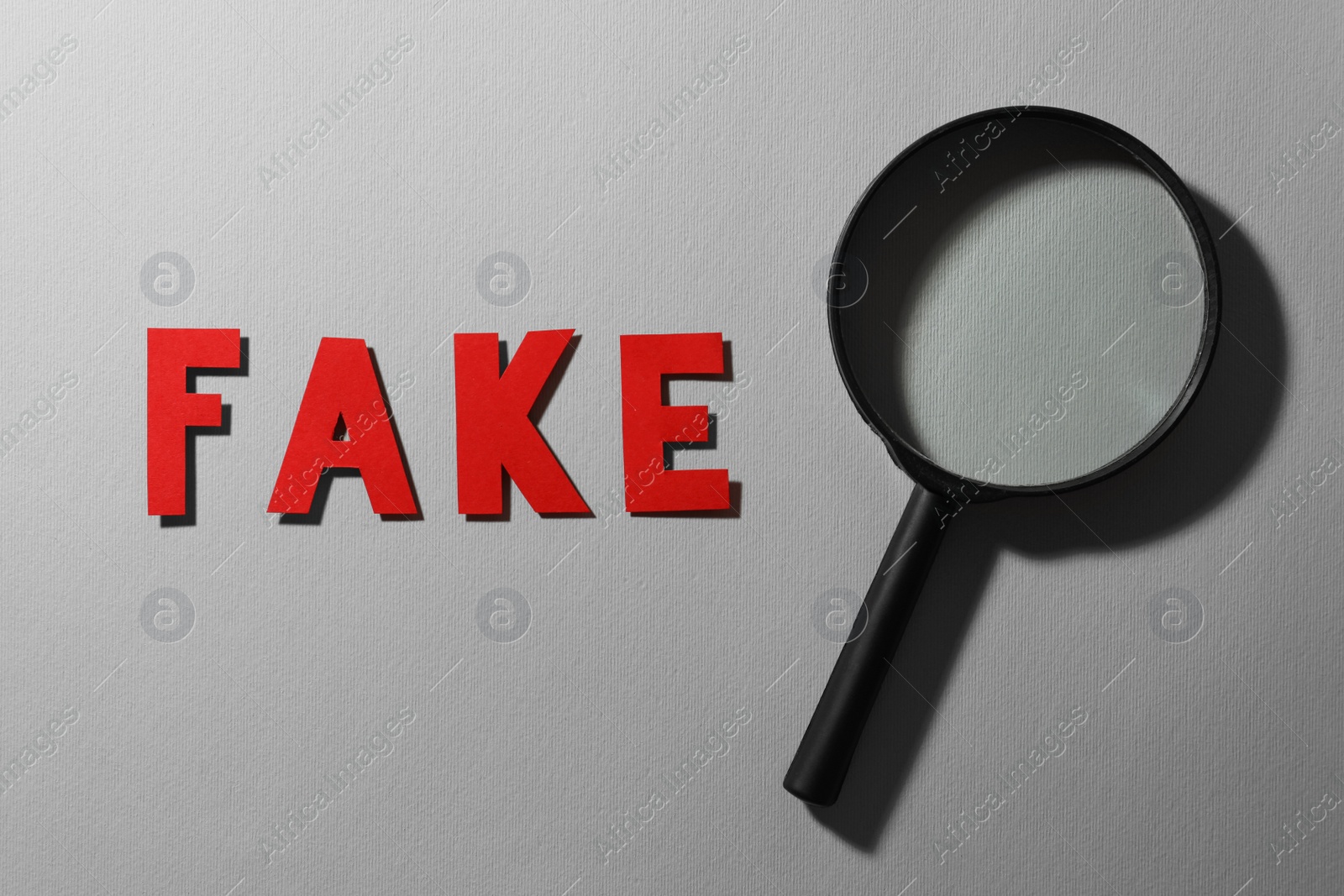 Photo of Word Fake made of red letters and magnifying glass on grey background, flat lay