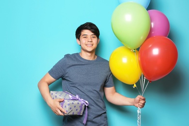 Young man with bright balloons and birthday gift on color background