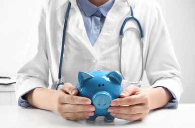 Photo of Doctor with piggybank at white table indoors, closeup. Medical insurance concept