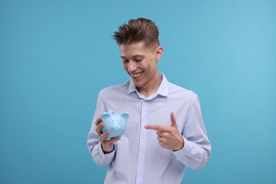 Photo of Happy man pointing at piggy bank on light blue background