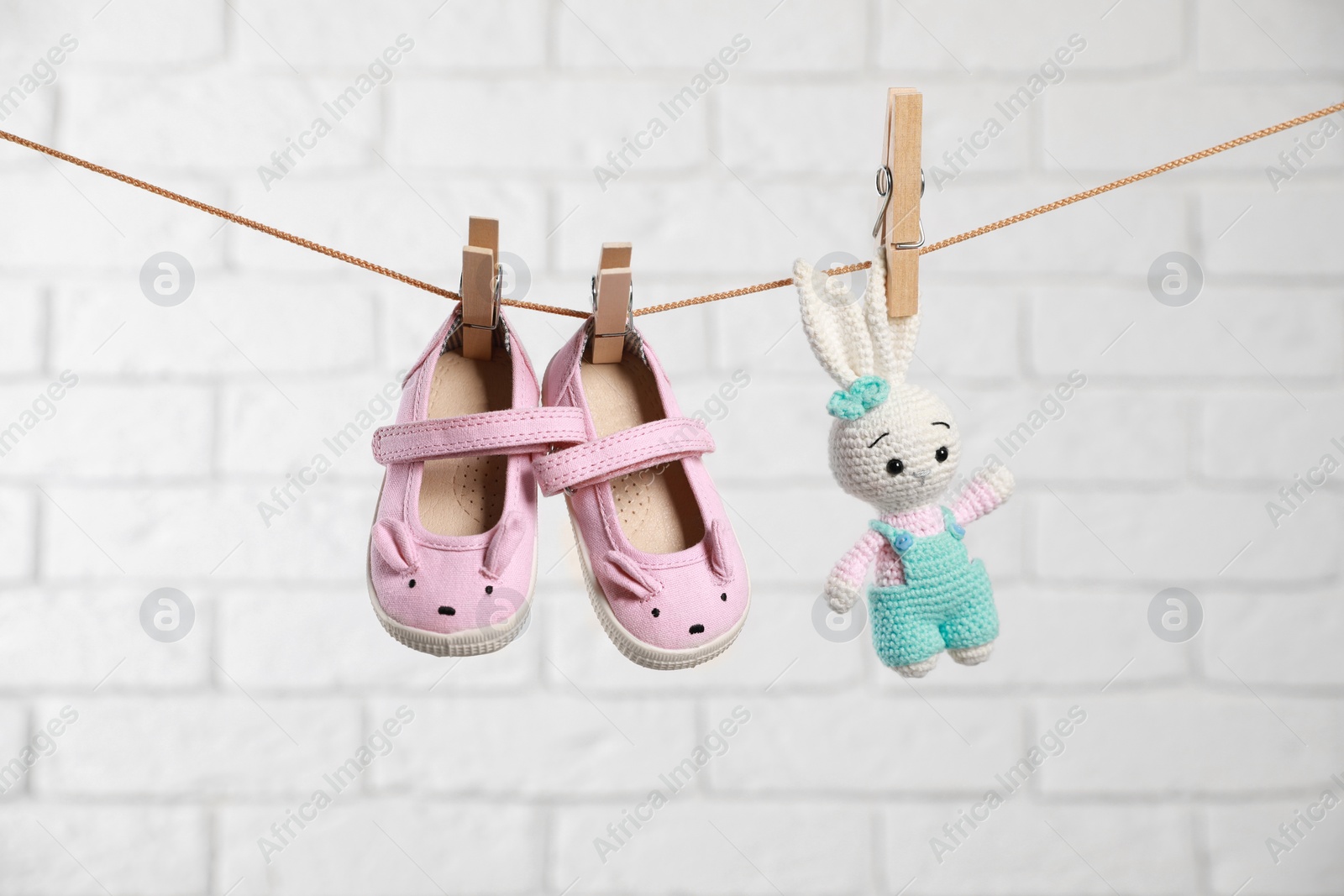 Photo of Cute pink baby shoes and crochet toy drying on washing line against white brick wall
