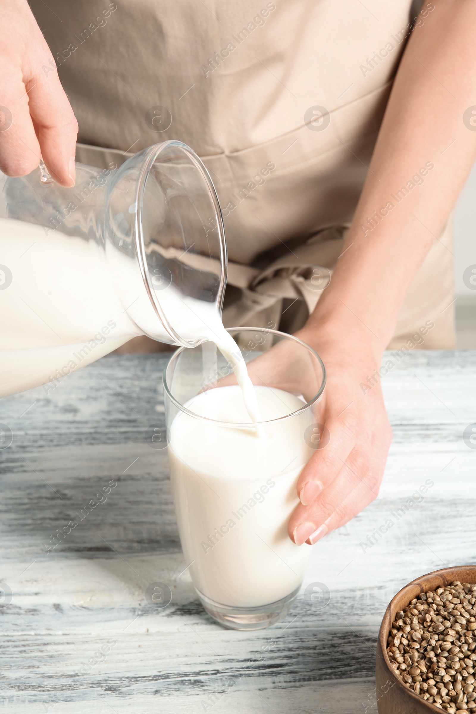 Photo of Woman pouring hemp milk into glass on table, closeup